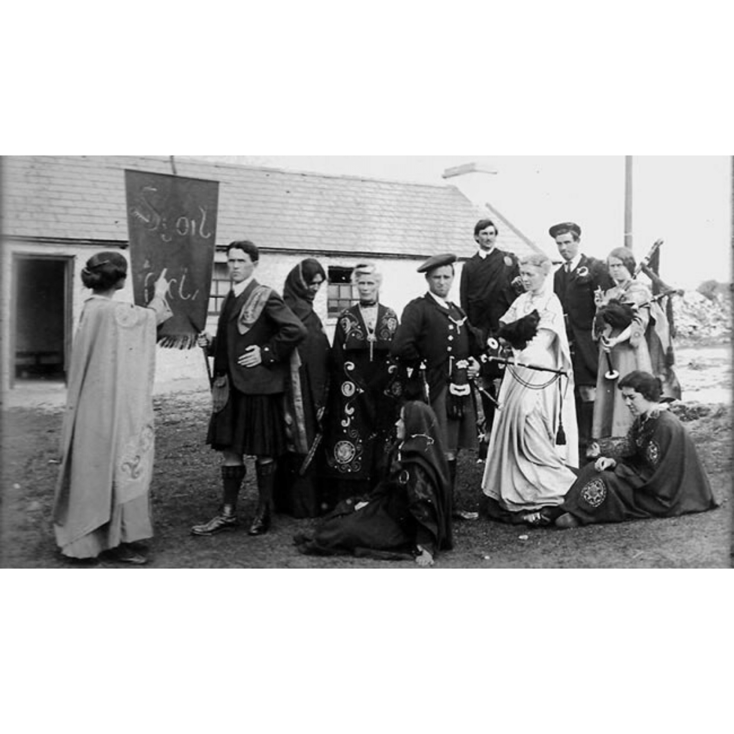 Early 20th-century Scoil Acla members in traditional Celtic robes outside a whitewashed Achill cottage